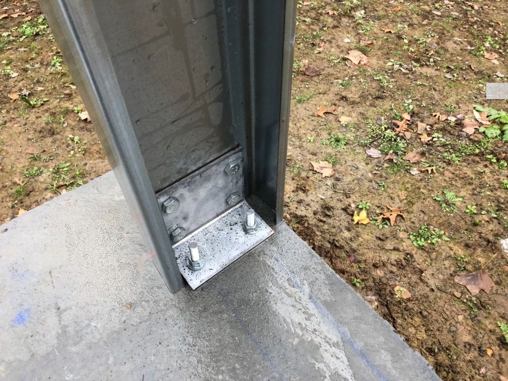 Cold-formed steel column base plate with anchor bolts mounted to concrete slab, showing light-gauge framing connection.