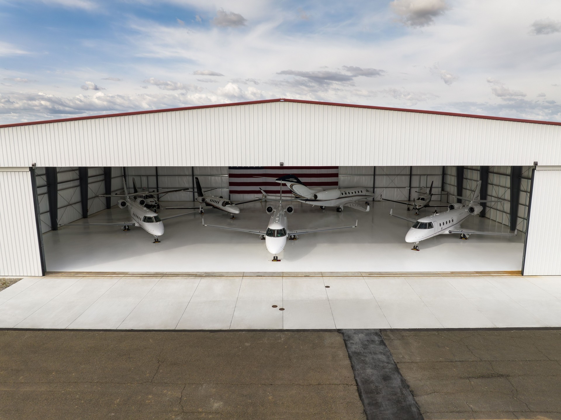 Exterior view of a steel airplane hangar with large open bay and private jets parked inside, showcasing aviation-ready cold-formed and red iron metal buildings.